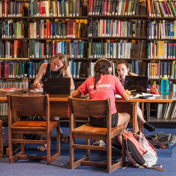 Three students study at a table in front of shelves of library books